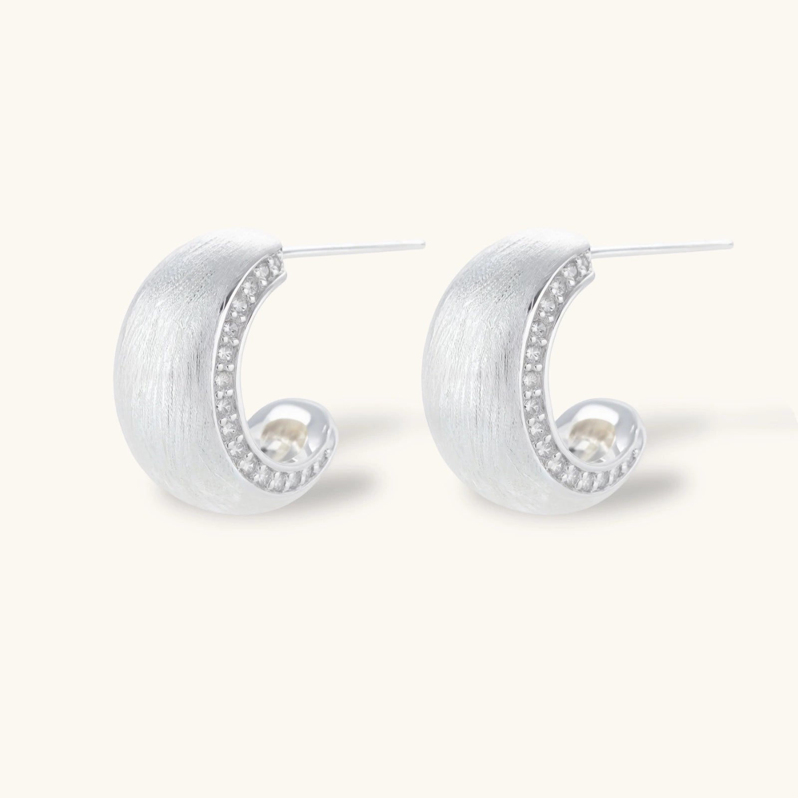 Close-up of small silver-plated hoop earrings with brushed texture and a row of sparkling zircon crystals on white background