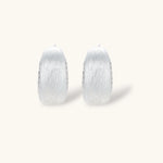 Close-up of small silver-plated hoop earrings with brushed texture and a row of sparkling zircon crystals on white background