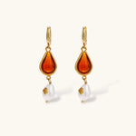 Gold-plated drop earrings featuring amber teardrops and white baroque pearls on light background.