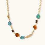 Statement necklace with gold chain, turquoise stones, amber beads, and wooden elements on cream background.