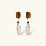 Gold-plated drop earrings with amber stones, teal beads, and wire-wrapped baroque pearls on cream background.
