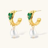 Gold-plated drop earrings with green heart charms and baroque freshwater pearls on neutral background.