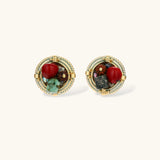 Circular gold-plated earrings with turquoise, coral, wood beads, and rope border detail on cream background.