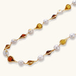 Gold-plated copper necklace with amber teardrop settings and white baroque freshwater pearls on cream background.