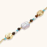 Gold-plated bracelet with baroque pearl centerpiece, turquoise and amber natural stones on adjustable chain against white background.