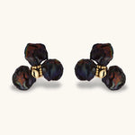 Dark iridescent baroque pearls arranged in flower pattern with 18K gold-plated center on cream background.