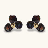 Dark iridescent baroque pearls arranged in flower pattern with 18K gold-plated center on cream background.