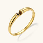 Polished gold bangle with two oval tiger's eye cabochons flanked by pavé diamond accents at center clasp.